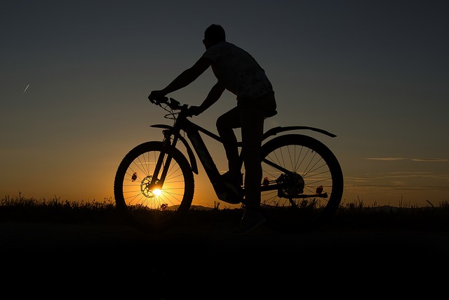 Silhouette of a mountain biker riding across desert slickrock at sunset near Moab, Utah, with the sky glowing orange and purple behind the red cliffs.