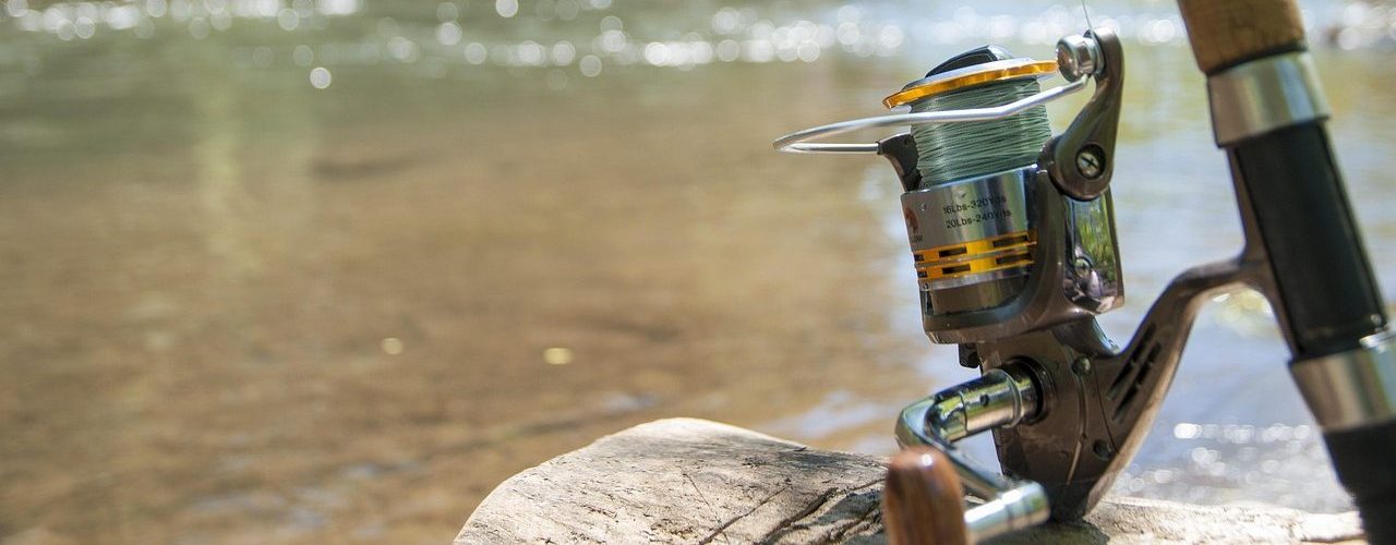 Fishing rod resting on a log beside a clear river with anglers in the background.