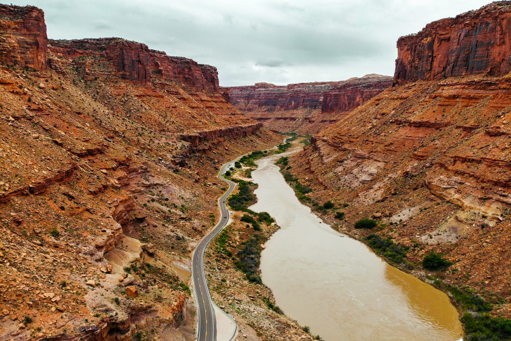 An elevated view shows a two-lane highway winding alongside the Colorado River through a deep red rock canyon.
