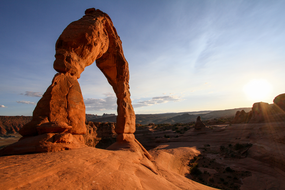 Delicate Arch glows orange in the setting sun, framed against a blue sky in Arches National Park.